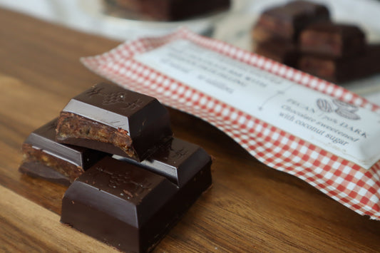 Dark chocolate bars stacked on a wooden surface with a red and white checkered bag in the background.
