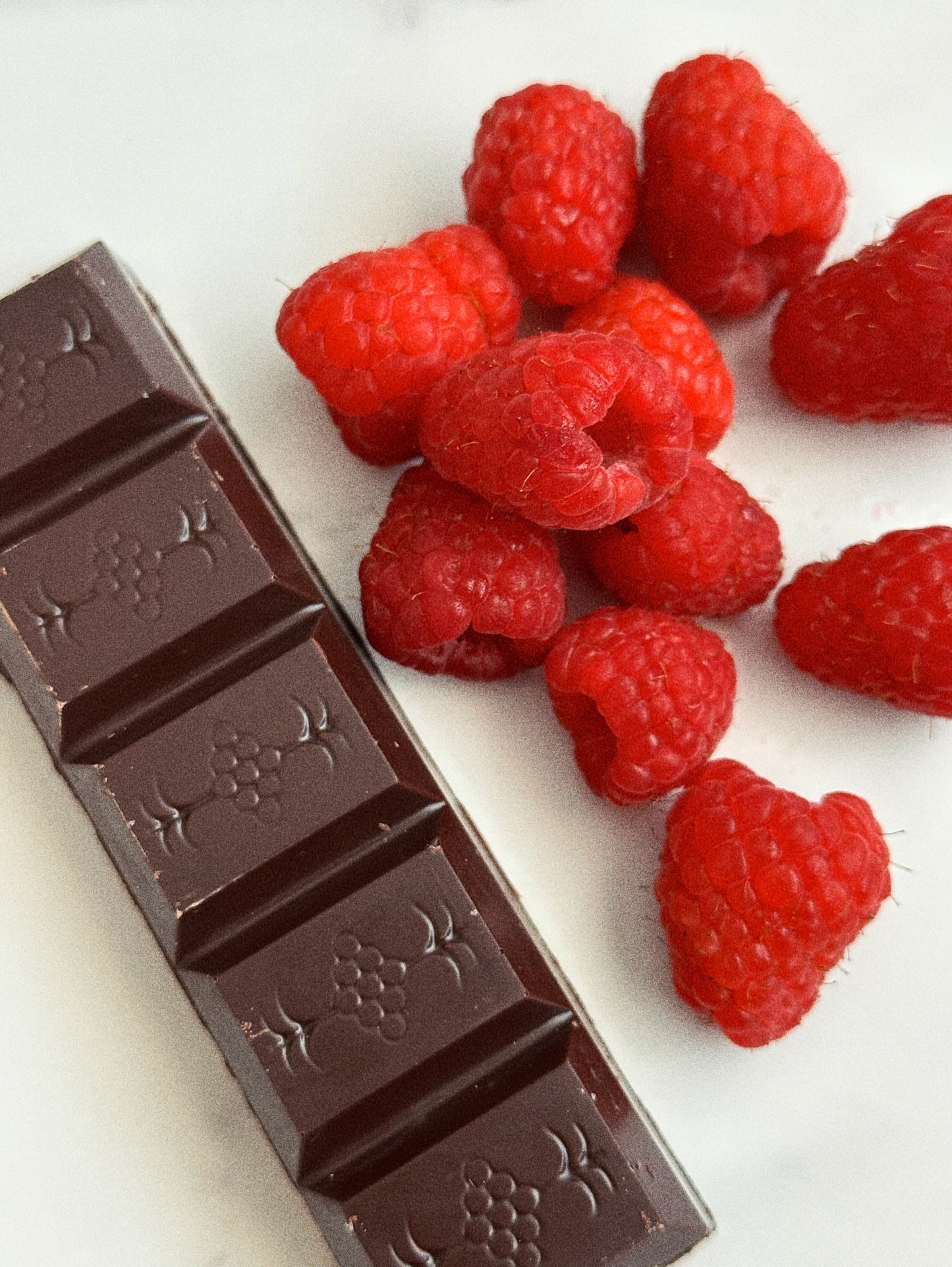 Chocolate bar with mild addictions logo next to fresh raspberries on a white surface