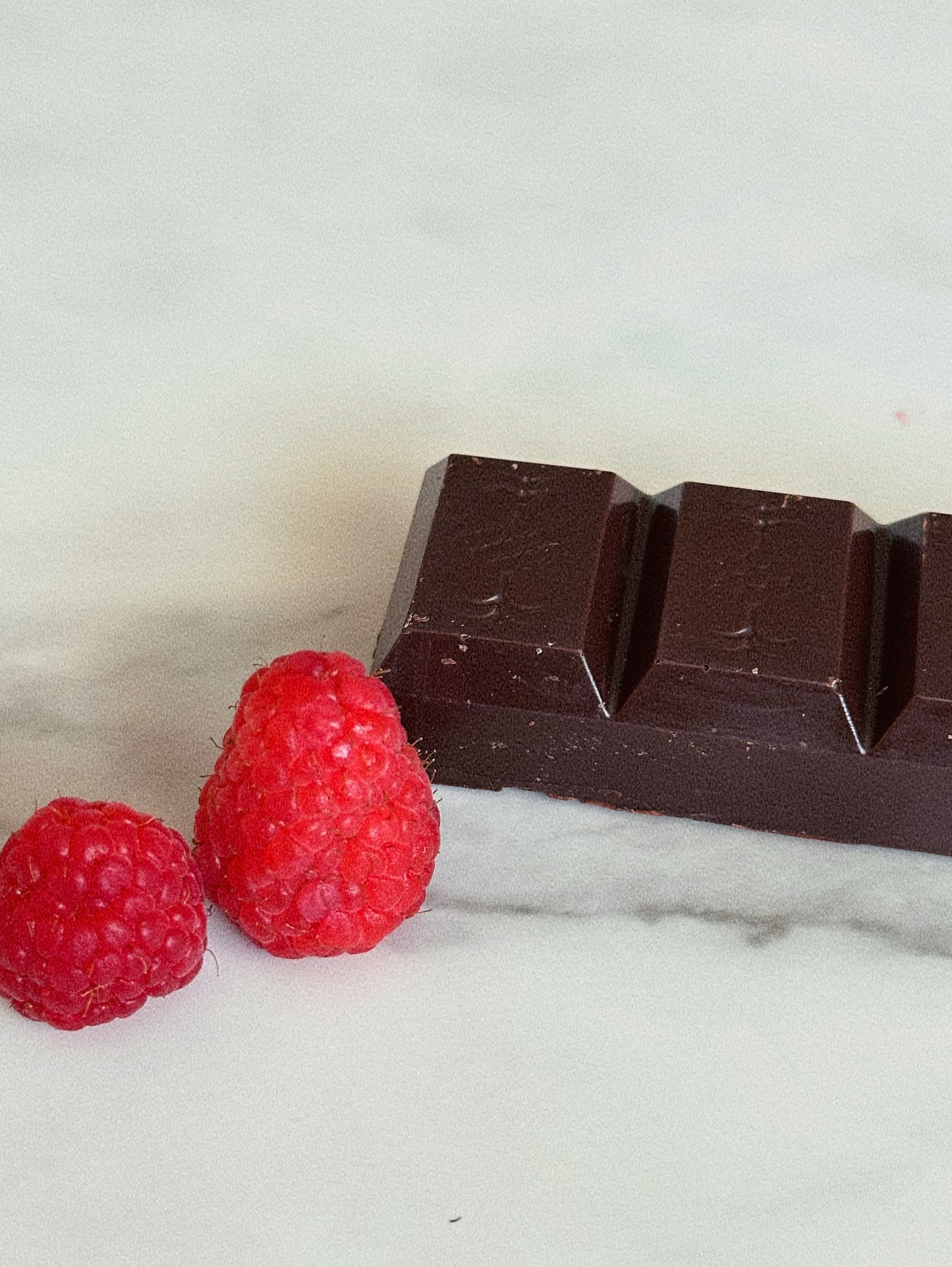 Dark chocolate bar with two raspberries on a marble surface