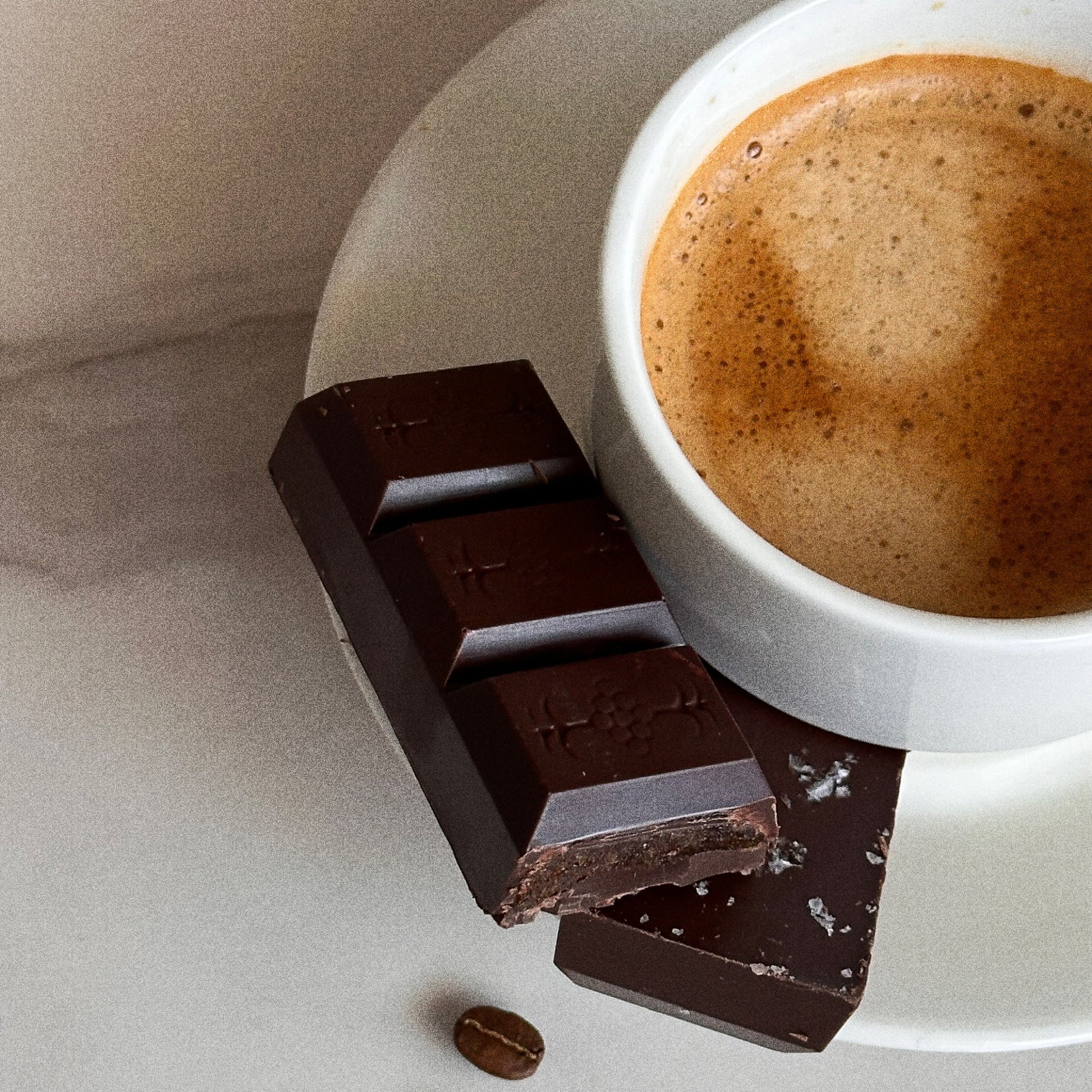 Dark chocolate bar with a cup of coffee on a light surface