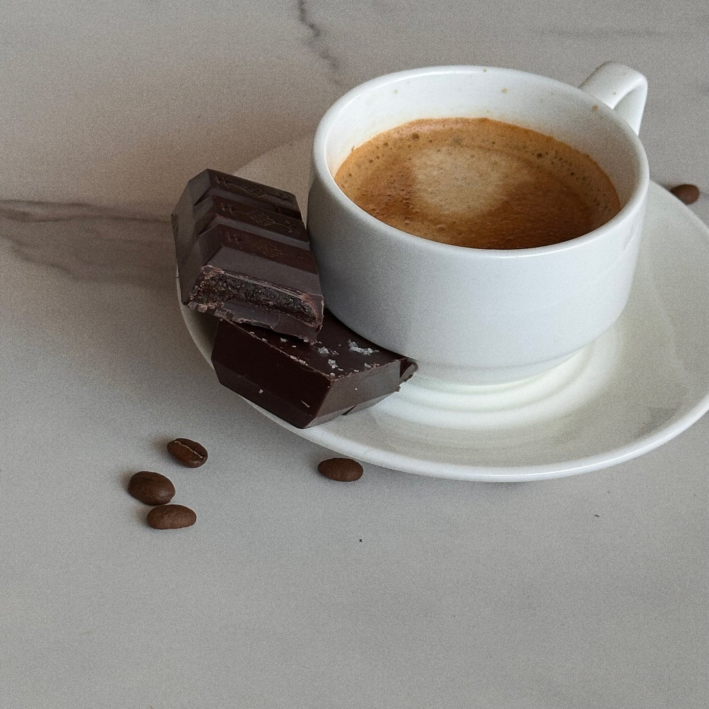 White cup of coffee with chocolate and coffee beans on a light surface