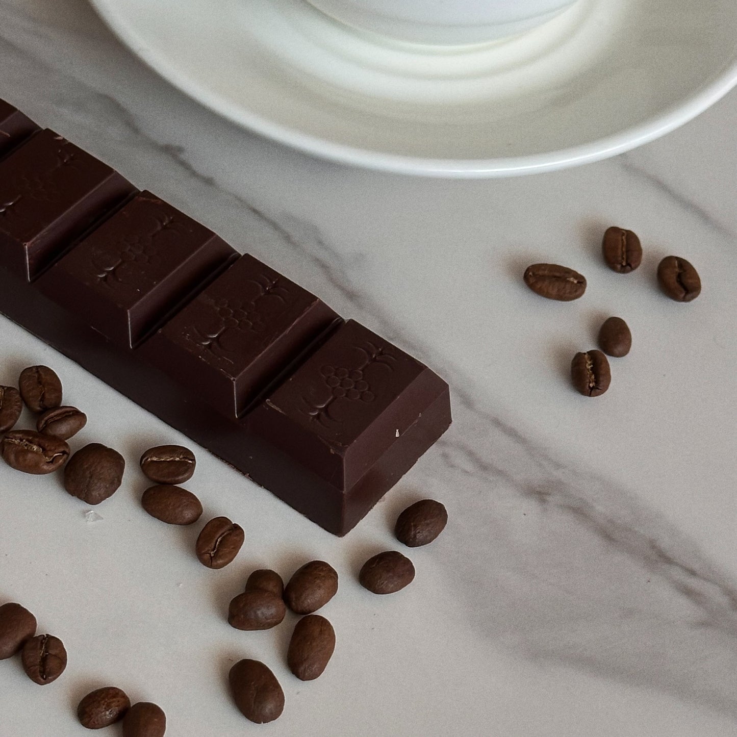 Dark chocolate bar with coffee beans on a marble surface