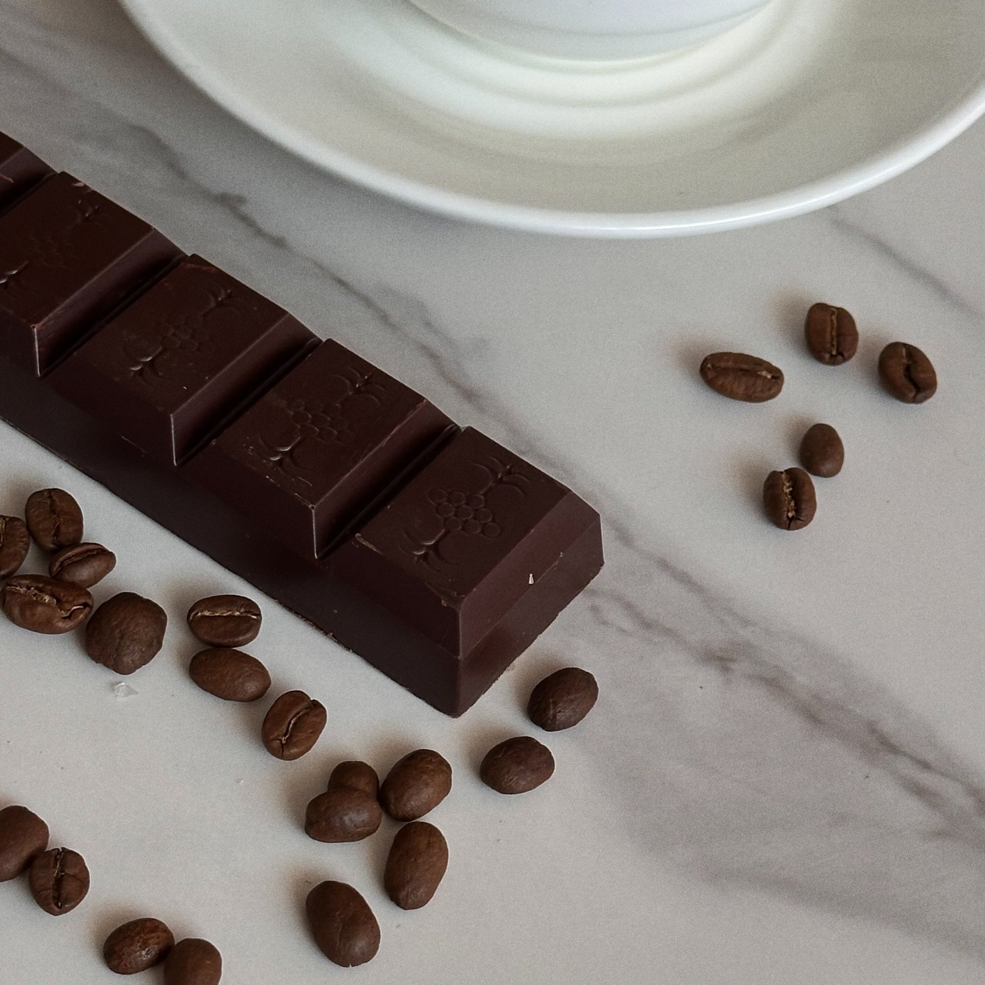 Dark chocolate bar with coffee beans on a marble surface